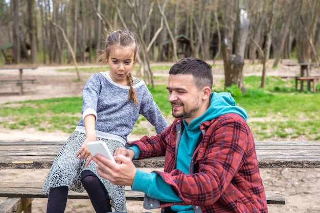 Papá y su pequeña hija miran el teléfono mientras caminan por el bosque.