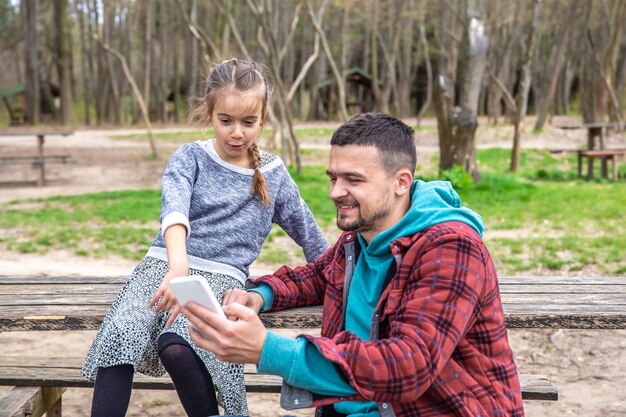 Papá y su pequeña hija miran el teléfono mientras caminan por el bosque.