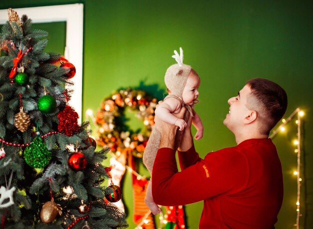 Papá tiene hijita en un traje de ciervo posando delante de un árbol de Navidad