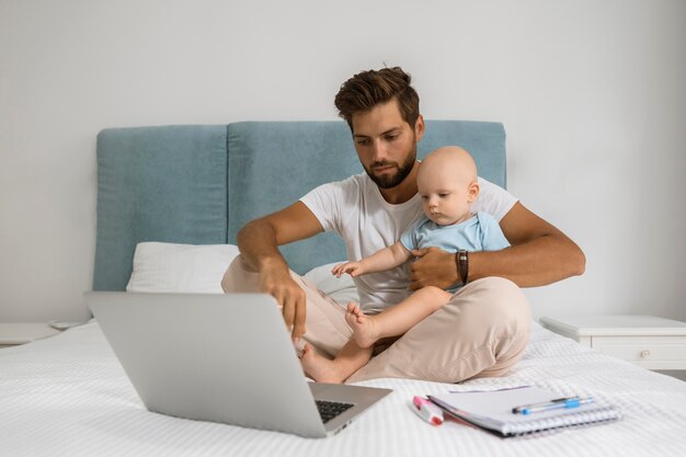 Papá trabajando en la computadora portátil desde casa durante la cuarentena con el niño