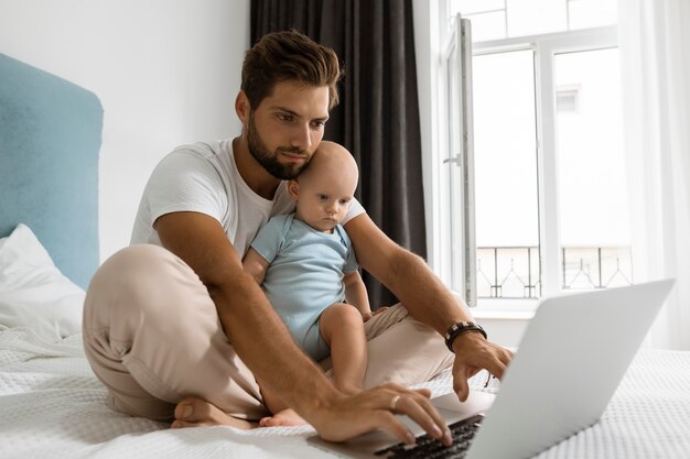 Papá trabajando en la computadora portátil desde casa durante la cuarentena con el niño