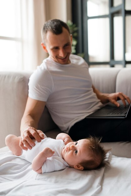 Papá usando la computadora portátil y tocando al bebé acostado en la manta