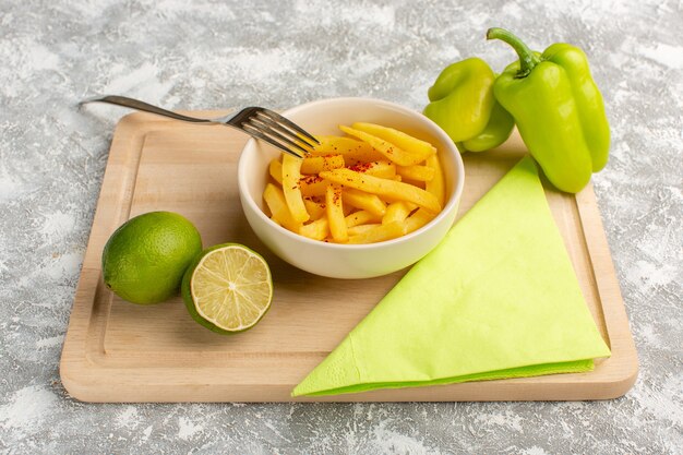 papas fritas dentro de la placa blanca junto con pimiento verde y limón sobre gris