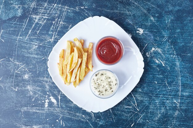 Papas fritas con salsas en un plato blanco.