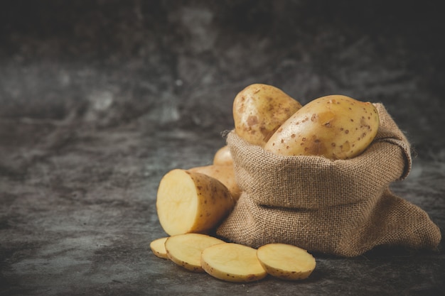 Papas en rodajas colocadas alrededor del saco de papa en el piso gris