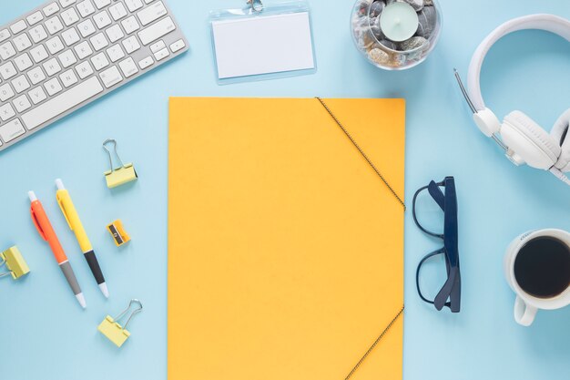 Papel amarillo en blanco con vela; teclado; auricular Taza de café y gafas sobre fondo azul