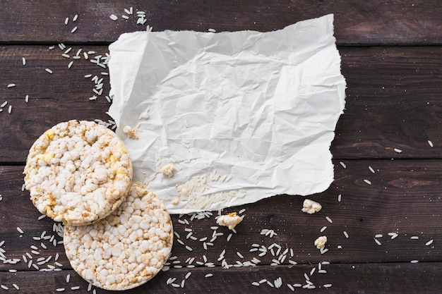 Papel arrugado con dos pasteles redondos de arroz inflado con granos en el escritorio de madera