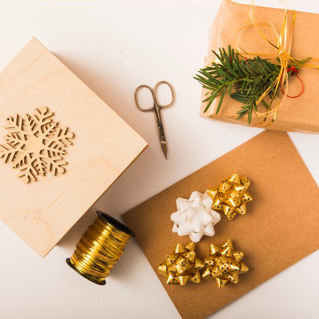 Papel de artesanía cerca del arco, cajas de regalo, tijeras, copo de nieve y cinta.