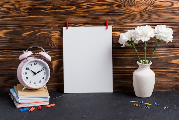 Foto gratuita papel blanco en blanco; florero; despertador y cuadernos contra fondo de madera.