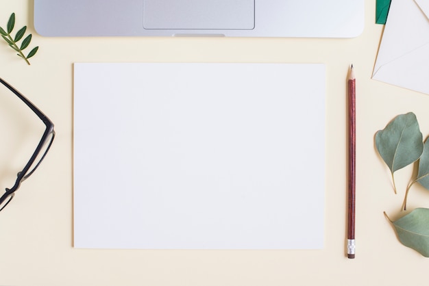 Papel blanco en blanco; lápiz; los anteojos; Hojas y laptop sobre fondo beige.
