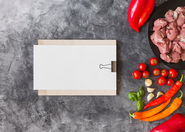 Papel blanco en blanco en el portapapeles con ingredientes para hacer carne sobre fondo texturizado