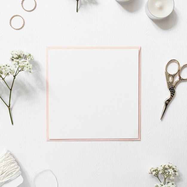 Papel blanco en blanco rodeado de anillos; gypsophila; cuerda; velas y tijera sobre fondo blanco