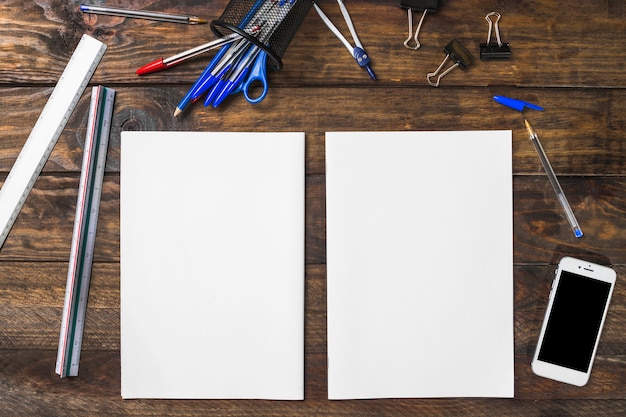 Papel en blanco blanco rodeado de artículos de papelería y teléfonos inteligentes en la mesa de madera