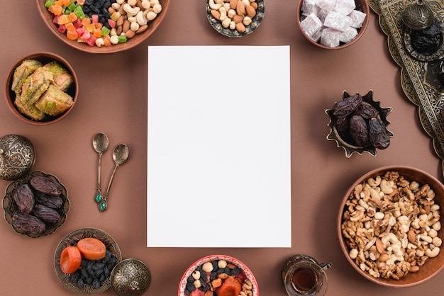 Papel blanco en blanco rodeado de frutos secos circulares; nueces; lukum; tazón de baklava sobre fondo marrón