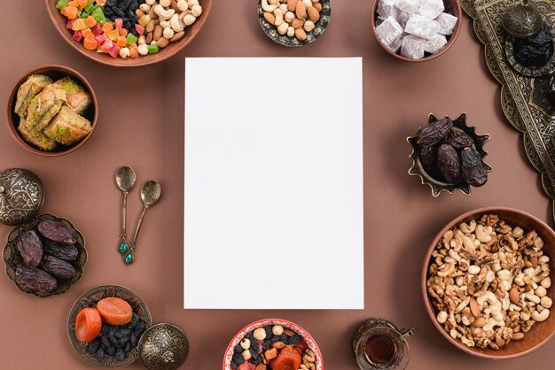 Papel blanco en blanco rodeado de frutos secos circulares; nueces; lukum; tazón de baklava sobre fondo marrón