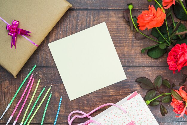 Papel en blanco blanco con velas; caja de regalo; flores y bolso de compras en la mesa