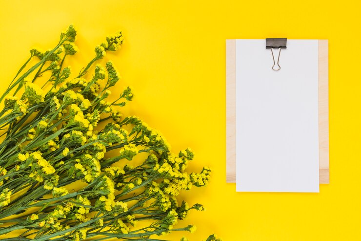 Foto gratuito papel en blanco en el clipboard con un ramo de flores contra un telón de fondo amarillo