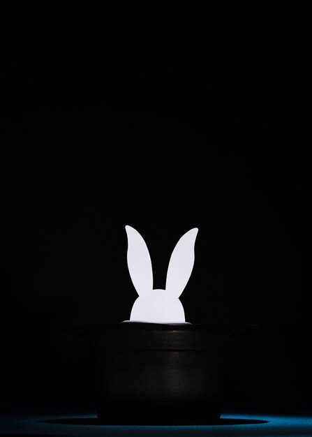El papel blanco cortó las cabezas del conejo en el sombrero negro superior contra fondo negro