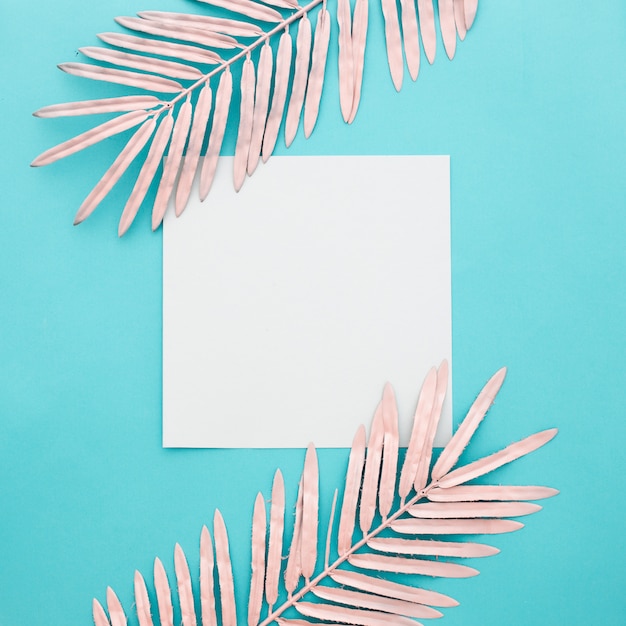 Foto gratuita papel en blanco con hojas de color rosa sobre fondo azul