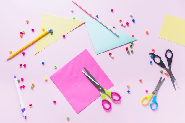Papel de colores lápiz; bolígrafo; cuentas y tijera sobre fondo rosa