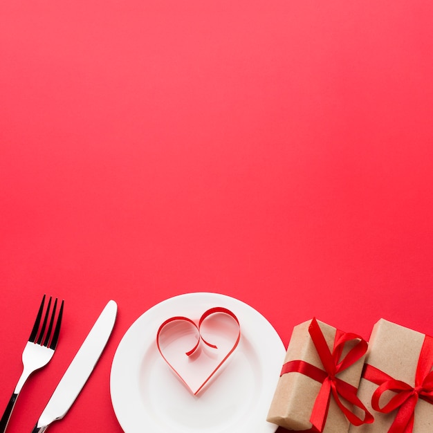 Papel en forma de corazón en un plato con regalos y cubiertos