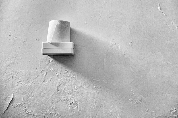 Papel higiénico colocado encima de una caja de plástico blanca con una pared blanca en el fondo