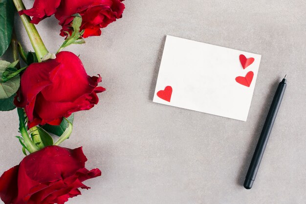 Papel con pequeños corazones cerca de pluma y flores