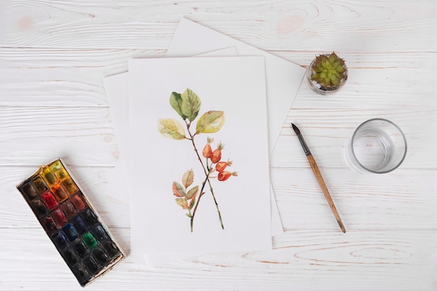 Papel con pintura vegetal cerca de vidrio, pincel y acuarelas.