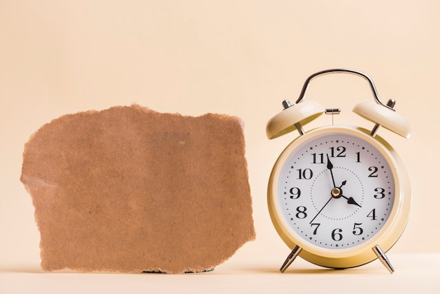 Papel rasgado marrón en blanco cerca del reloj de alarma contra el fondo coloreado