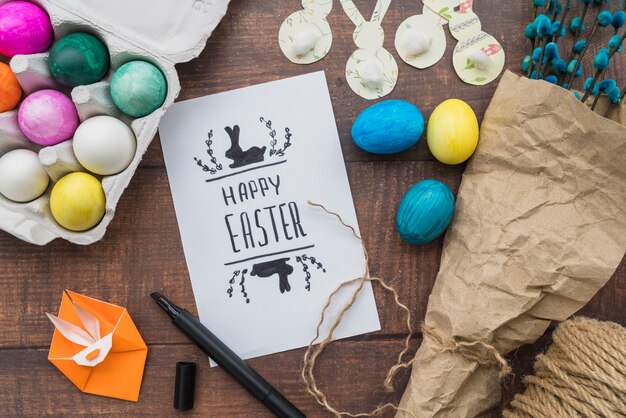 Papel con título cerca del conjunto de huevos de Pascua, ramitas de sauce y origami de conejo