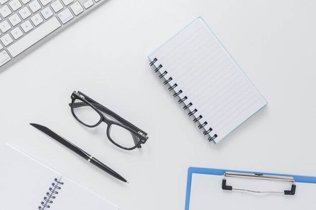 Papelería cerca de gafas y teclado en escritorio blanco