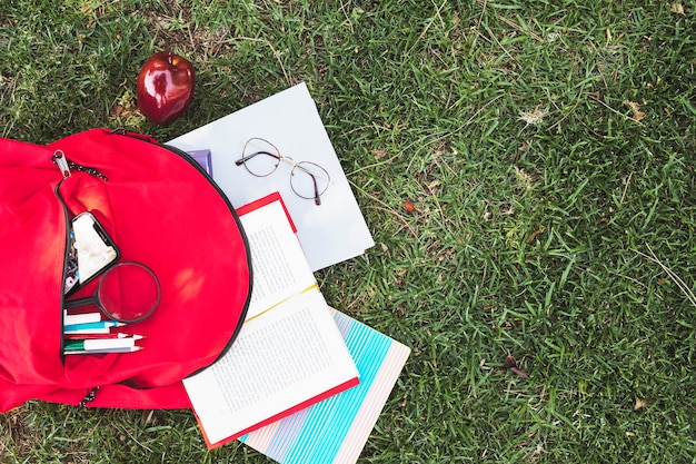 Papelería dispersa de mochila roja sobre hierba