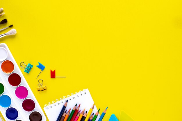 Papelería escolar de colores sobre fondo amarillo con copyspace.