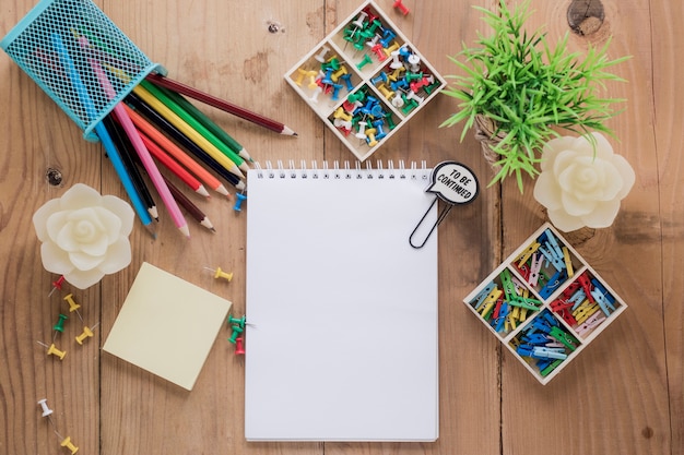 Papelería y planta alrededor de un cuaderno vacío