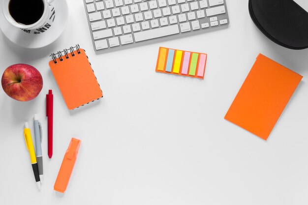 Papelerías coloridas con taza de café; manzana y teclado en escritorio blanco