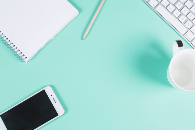 Papelerías con teclado; taza y teléfono celular en el fondo de color