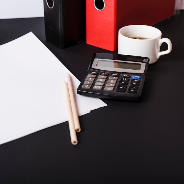 Papeles blancos en blanco; lapices archivos en papel; Taza de café y calculadora en escritorio negro