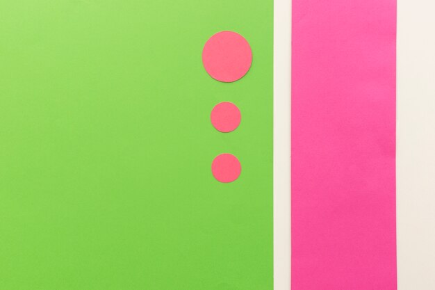 Papeles de forma de círculo rosa en diferentes tamaños dispuestos en papel de tarjeta verde