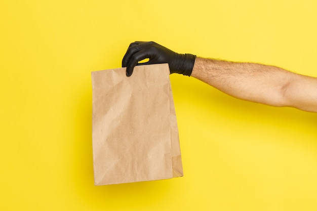 Paquete de alimentos de vista frontal sosteniendo por hombre en guantes negros sobre amarillo