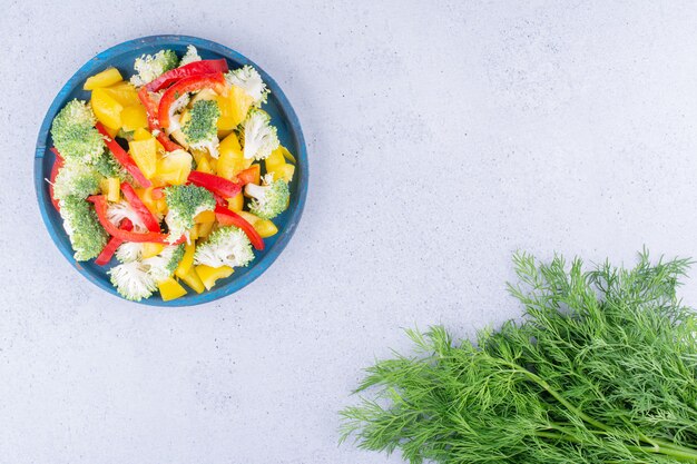 Paquete de eneldo junto a una fuente de ensalada sobre fondo de mármol. Foto de alta calidad