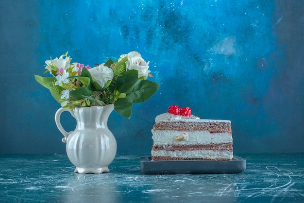 Paquete de flores junto a un pequeño trozo de tarta sobre fondo azul. Foto de alta calidad