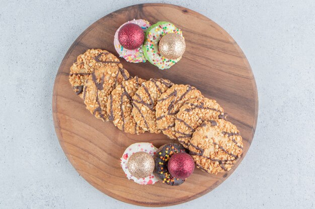 Foto gratuita paquete de galletas y donuts con adornos en un tablero sobre fondo de mármol.