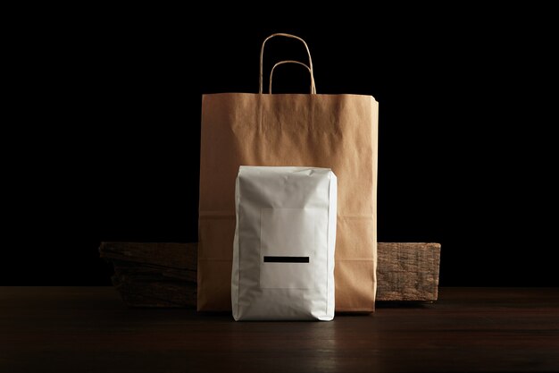 Paquete de mercancía para minoristas: gran bolsa hermética blanca con etiqueta en blanco presentada frente a la bolsa de papel artesanal y ladrillo de madera rústica en la mesa roja