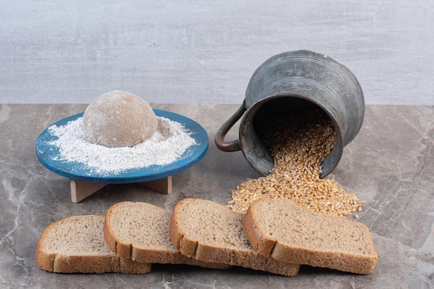 Paquete de rebanadas de pan, plato de harina y jarra de trigo derramada sobre fondo de mármol. Foto de alta calidad