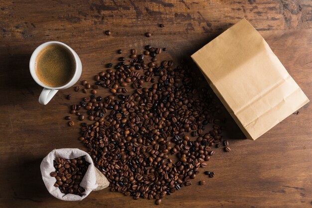 Paquete, saco y taza junto a los granos de café.