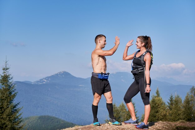 Un par de atléticos amigos sonrientes parados en la cima de la colina de la montaña