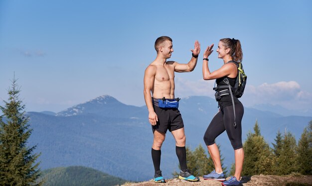 Un par de atléticos amigos sonrientes parados en la cima de la colina de la montaña