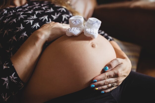 Par de calcetines de bebé en el estómago de la mujer embarazada en la sala de estar