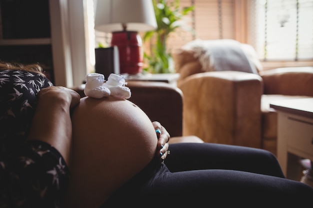 Par de calcetines de bebé en el estómago de la mujer embarazada en la sala de estar