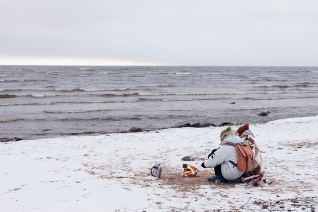 Par calentar junto al fuego en la playa durante un viaje por carretera de invierno